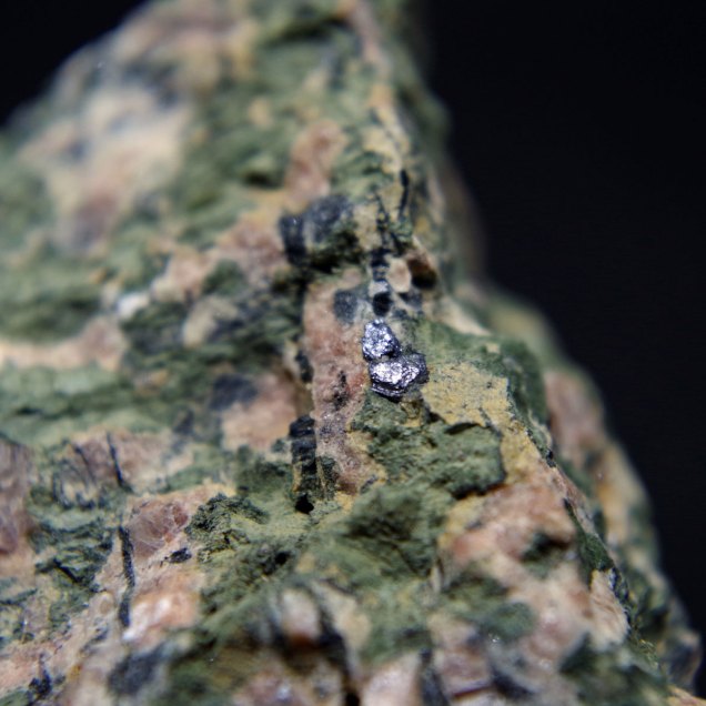 Molybdenite MoS2 in aegerine rich albite-microcline rock [rock containing pink microcline K(AlSi3O8), green pyroxene – aegirine NaFeSi2O6 and white albite Na(AlSi3O8)]; Dmitrievskii quarry, Oktyabr'skii Massif (Mariupol'skii), Azov Sea Region, Donetsk (Donets'k) Oblast', Ukraine; bigger crystal of molybdenite 4 mm