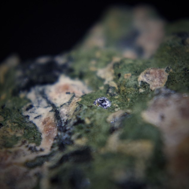 Molybdenite MoS2 in aegerine rich albite-microcline rock [rock containing pink microcline K(AlSi3O8), green pyroxene – aegirine NaFeSi2O6 and white albite Na(AlSi3O8)]; Dmitrievskii quarry, Oktyabr'skii Massif (Mariupol'skii), Azov Sea Region, Donetsk (Donets'k) Oblast', Ukraine; crystal of molybdenite 2 mm