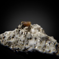 Orange-brown crystal of prismatic synchisite-(Ce) CaCe(CO3)2F on matrix; Wanni glacier - Scherbadung area, Kriegalp Valley, Binn Valley, Wallis, Switzerland; crystal 4 mm long