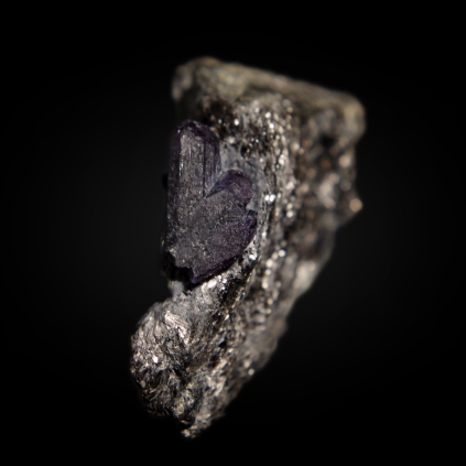 Dark, almost black, partially twinned chrysoberyl var alexandrite BeAl2O4 crystals with purple tint in artificial (incandescent light bulb) light embedded in schist matrix; Carnaíba mining district, Pindobaçu, Campo Formoso ultramafic complex, Bahia, Brazil; crystal 13 x 7 x 3 mm