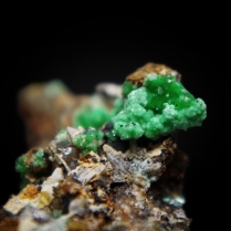 Green clusters of transparent annabergite Ni3(AsO4)2•8H2O crystals forming radiating cluster of thin blades; Km-3 Mine, Lavrion, Lavrion District Mines, Lavrion District, Attikí Prefecture, Greece; FOV: 15 mm